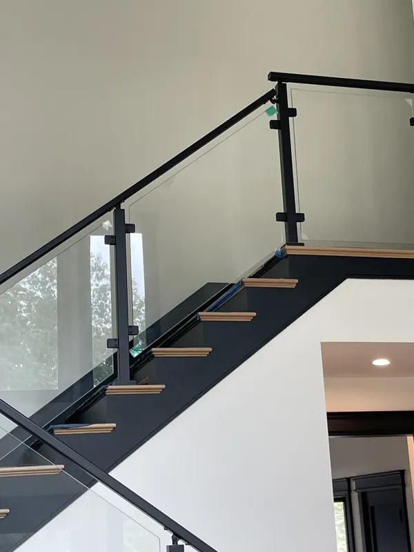 Glass railing with black posts on the upper flight of an interior staircase