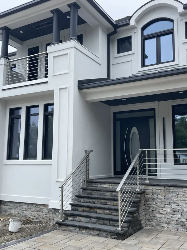 Horizontal metal railings on the front stairs and upper balcony of a modern home