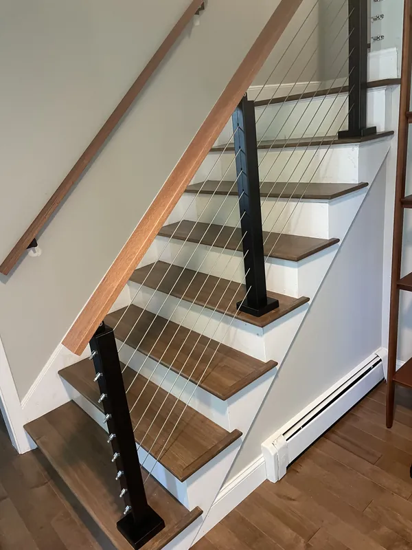 Cable railing with black posts and a wood handrail on a wood staircase