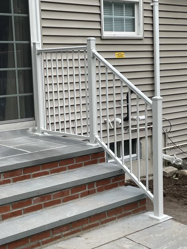 White stair railing with vertical balusters beside a brick entrance