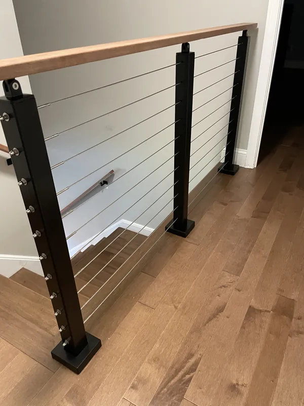 Cable railing with black posts and a wood handrail at an upstairs landing