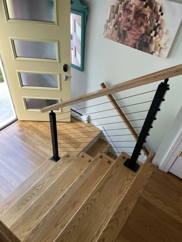 Interior cable stair railing with black posts and a natural wood handrail